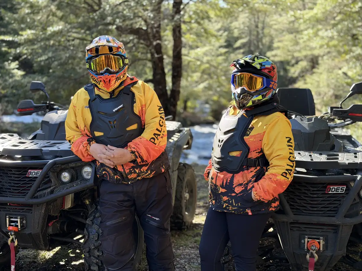 Dos integrantes de la familia de Palguín ATV Tour con la chaqueta de la marca puesta, de pie junto al río y a las dos cuatrimotos